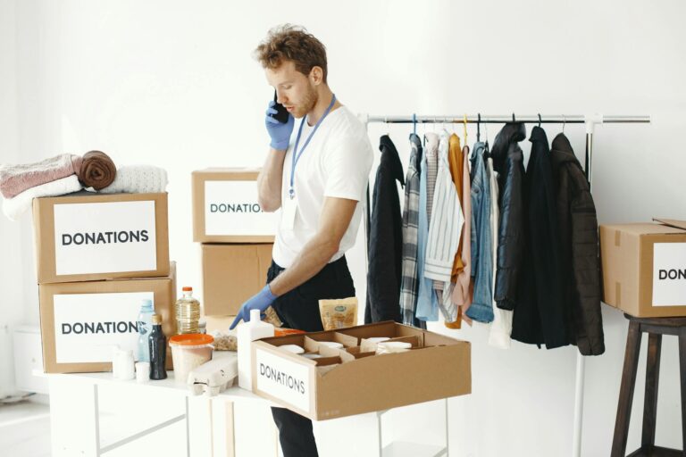 A volunteer organizes donation boxes and clothes while making a phone call in a bright room.
