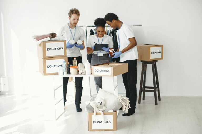Three volunteers organize donation boxes filled with essentials in a bright indoor setting.